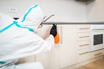 Exterminator in work wear spraying pesticide with sprayer. Selective focus.
