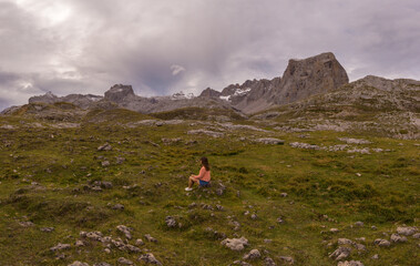Beautiful young woman sitting next to stunning summits of Mounts Pena Remona, Torre de Salinas, La...