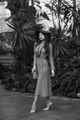 Full-body portrait of woman in knitted dress and hat posing in glasshouse