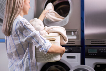 Housework: woman loading clothes into washing machine. caucasian lady enjoys cleaning process. focus on towels in basket