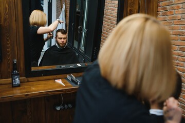 Stylish man sitting barber shop Hairstylist Hairdresser Woman cutting his hair Portrait handsome happy young bearded caucasian guy getting trendy haircut Attractive barber girl working serving client