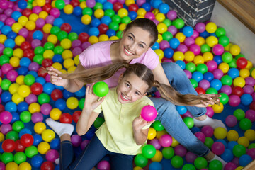 Fototapeta na wymiar Portrait of cheerful teen girl and her young mother spending time in ball pond at amusement park, top view