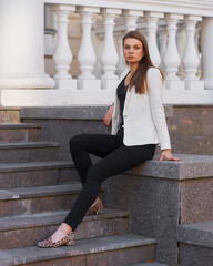 Young woman in black shirt, jeans and white blazer walking and posing outdoors on a summer day. Sun backlight. Outdoor portrait
