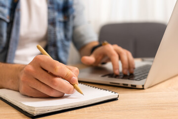 Fototapeta premium Cropped image of a young man working on his laptop in a coffee shop, rear view of business man hands busy using laptop at office desk, typing on computer sitting at wooden table
