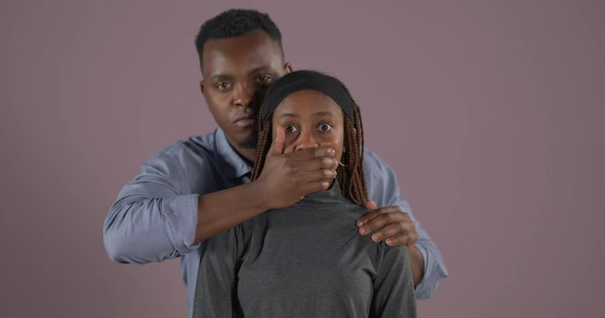 Portrait of African couple. Man covering mouth of scared woman and looking at camera. Domestic violence. Abuse in relationship.