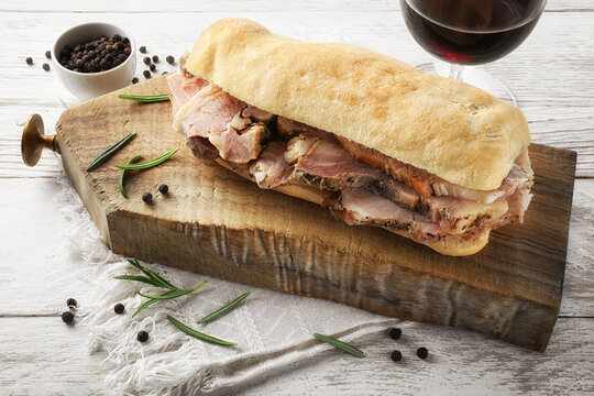 Porchetta sandwich with red wine, rosemary and peppercorns on white wooden table.