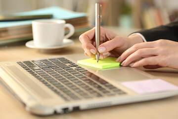 Teleworker writing sticky note on a laptop at homeoffice