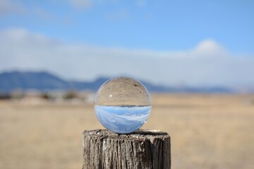 Glass lens ball showing inverted reflection of mountains and farm fields with blue sky and clouds...