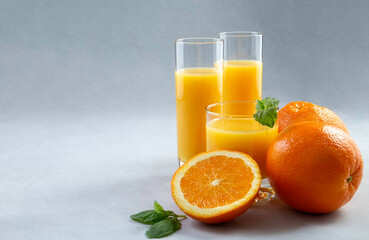 Fresh oranges and 100% orange juice in glasses on an gray background. Close-up. Copy space. Detox