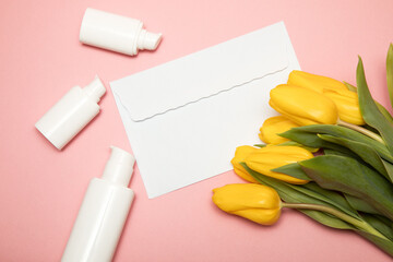 Yellow tulips on pink background with copy-space envelope and cosmetic bottles containers. Mock up. Happy mother's day, women's day congratulations concept