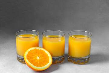 Natural 100% orange juice in a glass on a gray background. Citrus drink. Three glasses. Detox. Copy space.