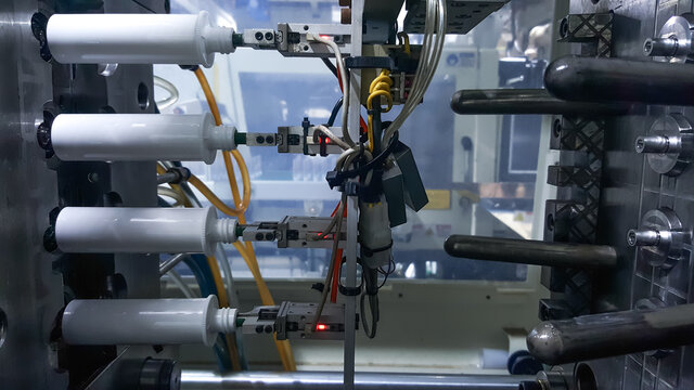 Robot arm holding plastic bottles, on the background of injection molding machines, in the working line of the plastics factory.