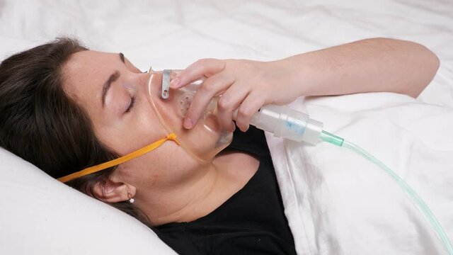 young woman in a mask lies on the bed and begins to cough and gasp.