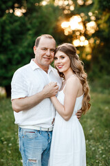 Young loving couple hugging on the green grass in the park. Beautiful woman and man gently touch each other. Beautiful couple in love. girl in the dress and the guy in the shirt. valentines day
