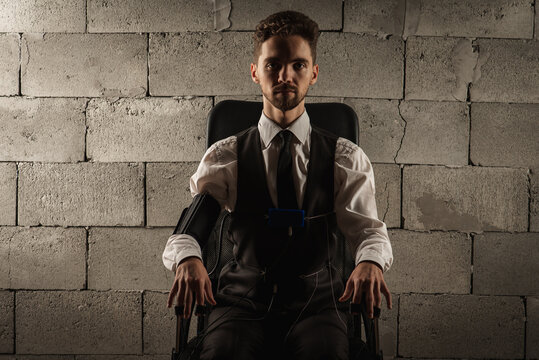 Concentrated, pensive, man in a gray room sitting on a chair, testing on a polygraph, has sensors for passing a polygraph, sitting on a gray brick wall background. The concept of truth, polygraph