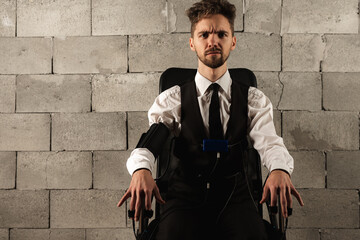 Fototapeta na wymiar frightened, worried, pensive, man sitting on a chair, testing on a polygraph, wearing sensors to pass a polygraph, sitting on a background of gray brickwork, looking straight