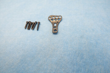 an explanted titanium plate and 4 titanium screws for the treatment of a radius fracture are lying on a light blue support