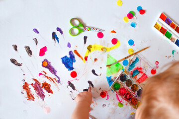 hands of a child drawing with paints on a white background on top. Colorful confetti. Close-up