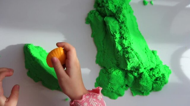 Close up of children's hands playing with green kinetic sand on white table; selective focus