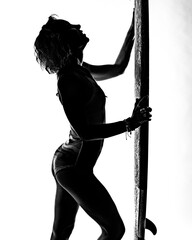 Black and white silhouette of a very fit surfer girl holding a surfboard