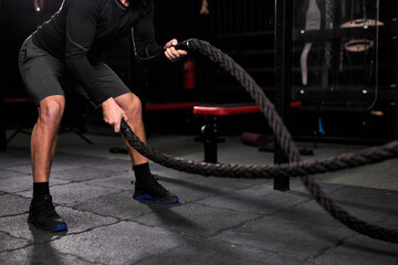 Naklejka premium Cropped athletic man doing cross fit exercises with rope at gym, concentrated and focused on training, workout. people and sport, cross fit concept
