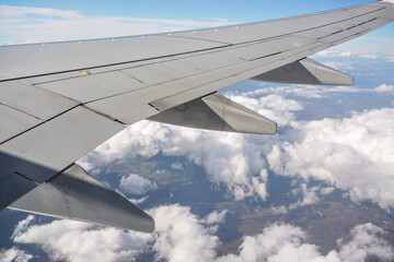 Fototapeta na wymiar View from passenger window of commercial airplane, clouds on blue sky visible under aircraft wing