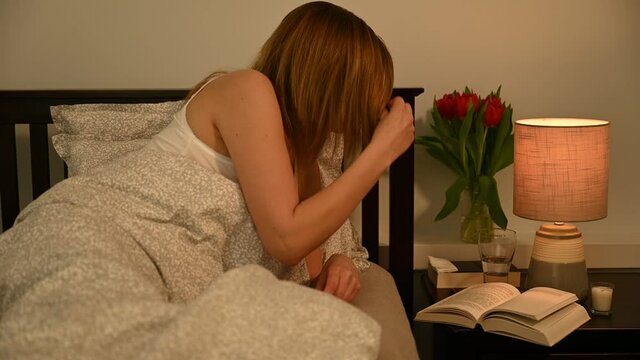 Attractive middle-aged woman in bed has just finished reading a book. Now she wants to fall asleep quickly, so she takes a sleep pill, turns off the light on the bedside table and tries to sleep.