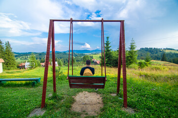 The guy tourist sit on the swing and enjoy amzing nature landscape of summer Karpaty mountains