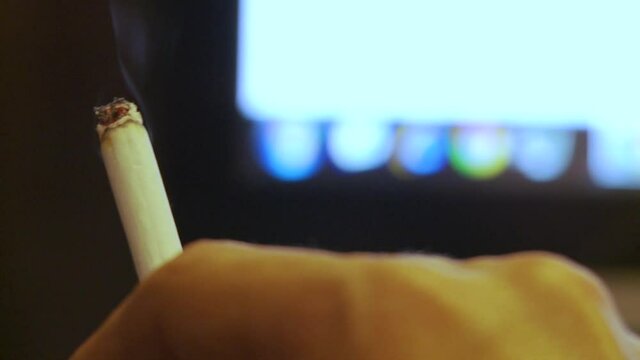 Close up shooting on an addicted to online gaming's hand moving or typing in front of a computer screen while holding a cigarette.