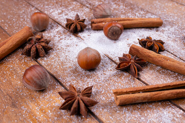close-up side view of asterisks, nuts and cinnamon sticks lie on the powder, on the background of wooden planks