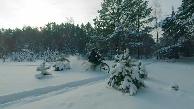 Cyclist in Black Clothes, Helmet and Snow Glasses Riding on Electric Bike in the Snow in Winter Forest. E-Bike Riding and Drifting at Cold Sunny Day - Super Slow Motion
