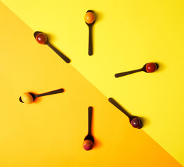 Arrangement of six chocolate spoons with marzipan fruit shaped candies in different colors and shapes - lemon, plum, orange, apple against diagonal of yellow and orange background. Taken from above.