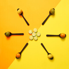 Arrangement of six chocolate spoons with marzipan fruit shaped candies in different colors and shapes - lemon, plum, orange, apple against diagonal of yellow and orange background. Taken from above.