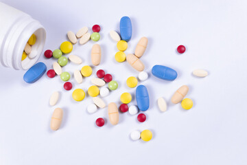 top view of the tablets pouring out of the jar onto a white surface, but some remained in the jar