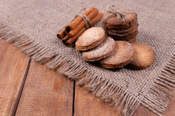 side view at an angle of a stack of cookies tied with a string, cinnamon sticks tied with a string, four cookies lying on top of each other, all this lies on a gray rug edged with fringe
