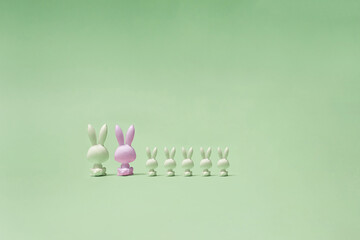 Fototapeta na wymiar Seven toy rabbits in white and pink colors sitting and staring in pastel green distance. Photo of bunnies' backs.