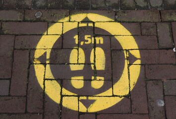 Yellow Painted Keep Your Distance Warning with Shoes in a Circle and Arrows on a Pavement in Amsterdam