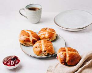 Traditional English Easter Hot Cross Buns on a plate with jam and tea cup