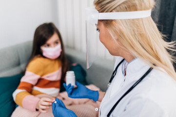 Doctor with shield on her face is giving pill to an ill girl. Coronavirus, Covid-19 concept.