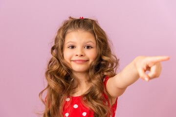 A little girl in a red dress points her finger to the side.