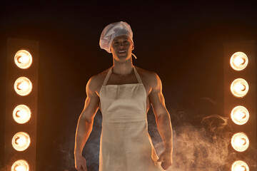 Portrait of muscular chef wearing white apron and cheef hat,  on smoky background
