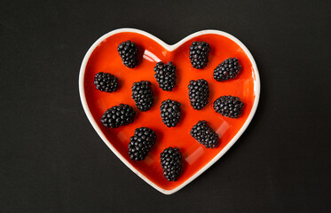 Valentine's Day. Red heart-shaped plate with large black berries on a black background.