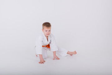 little boy in a white kimono does a stretch on a white background with space for text