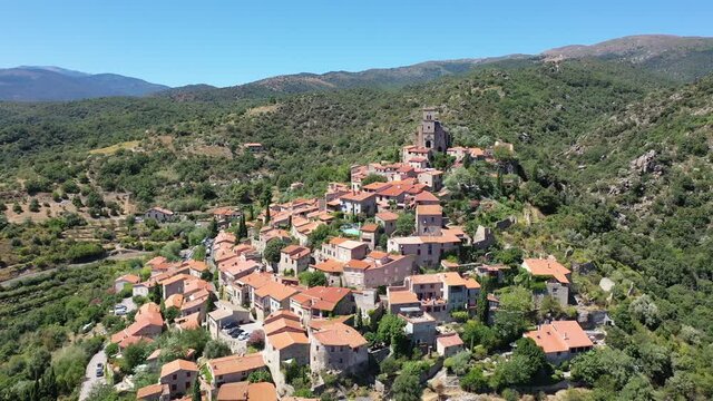 General summer view of picturesque French village of Eus in natural region of Conflent with tightly grouped houses, medieval church and castle ruins on top of hill