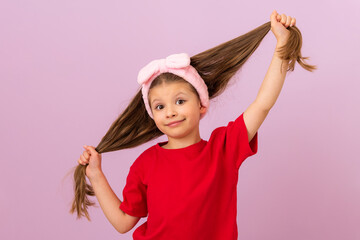 A little girl in a red T-shirt pulls her hair in different directions.