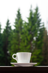 The white mug of dark hot morning coffee on wooden fence with forest background