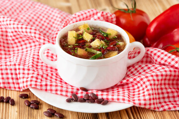 Traditional bean soup with vegetables and potatoes on a wooden background with garlic.