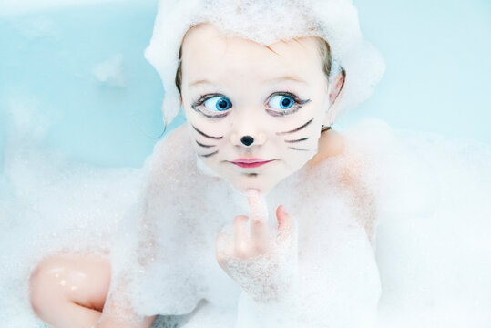 Portrait of a girl with whiskers drawn on her face sitting in the bath covered in soap suds