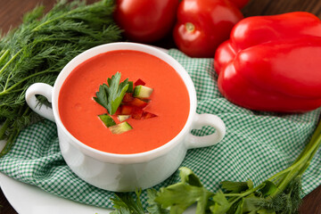 Spanish gazpacho soup on a wooden background with tomatoes and herbs.