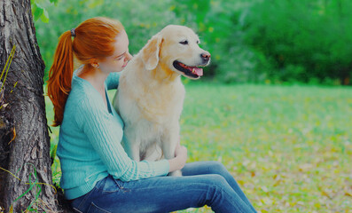 Happy woman sitting with her Golden Retriever dog on a grass in a park